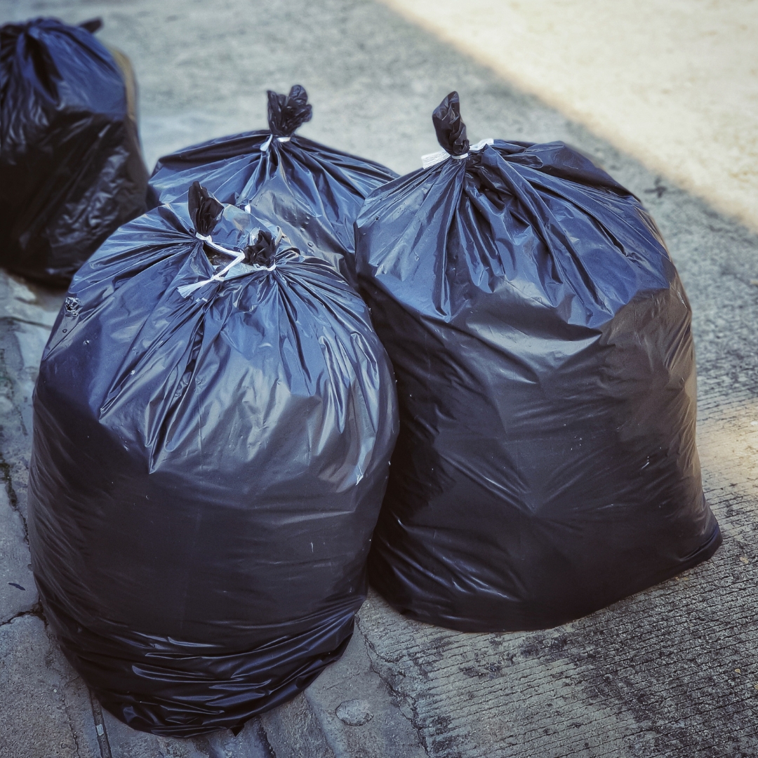 Four black trash bags drawn closed at the curb