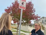 Crime Prevention Specialist is in front of a Neighborhood Watch sign while writing on a clip board.